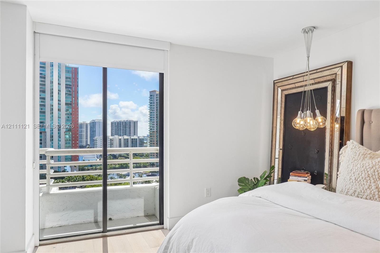 Floor-to-ceiling glass sliding door, private balcony with metal railing, multi-bulb pendant lighting fixture, and wood-finish flooring