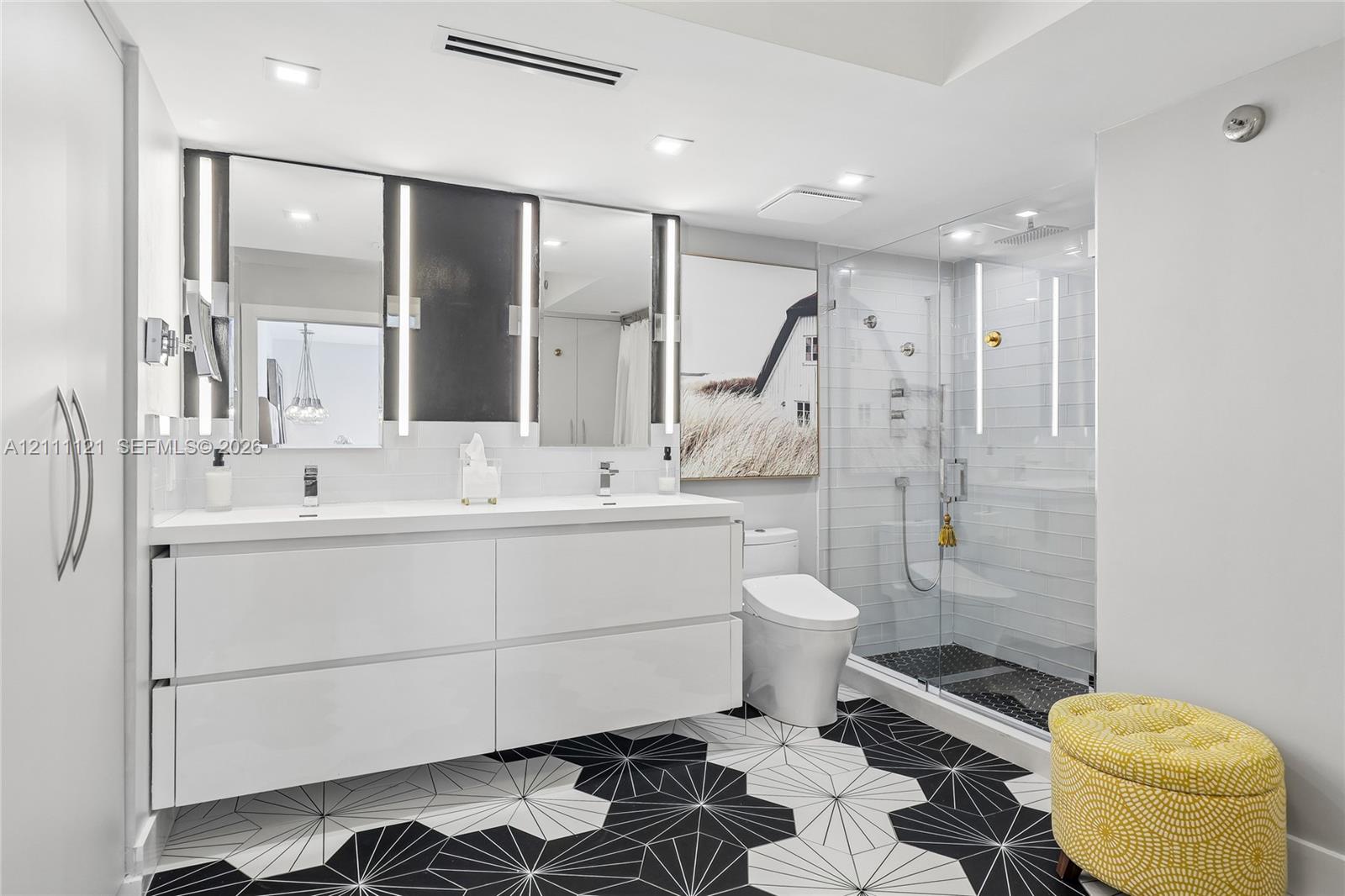 Floating double vanity with integrated sinks, geometric patterned floor tile, glass-enclosed shower with horizontal wall tile, and recessed lighting