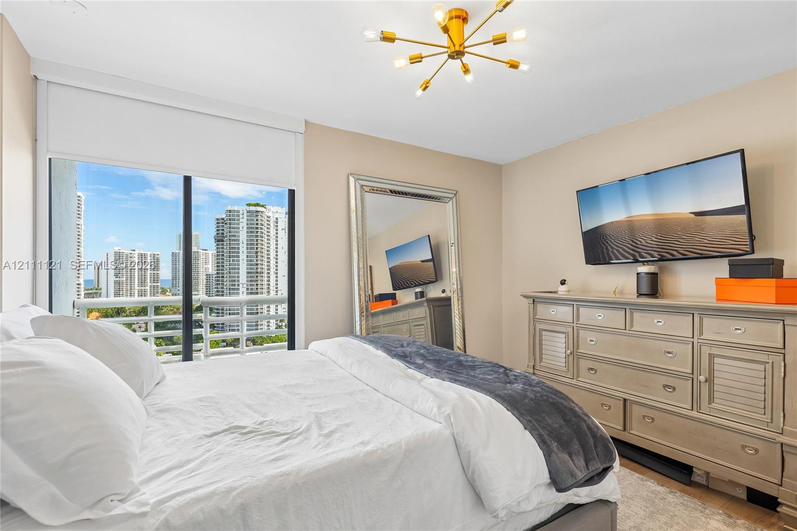 Floor-to-ceiling sliding glass door, private balcony, brass-finish multi-arm light fixture, and neutral wall palette