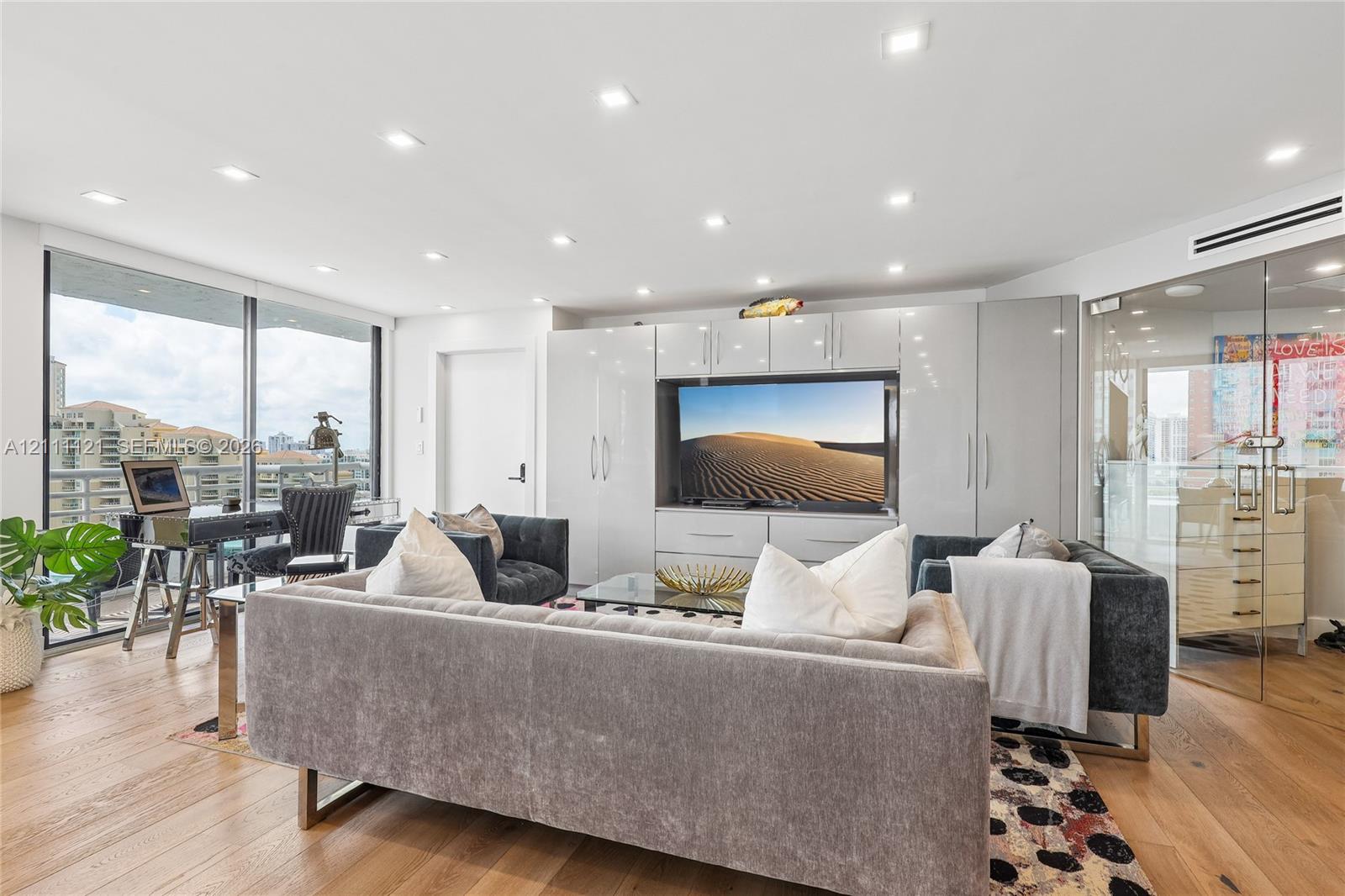 Living area featuring wood-finish flooring, recessed lighting, floor-to-ceiling windows, integrated white cabinetry, and a glass-enclosed partitioned space