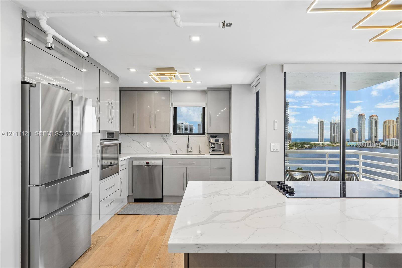 Modern kitchen featuring high-gloss cabinetry, stone-surface countertops with waterfall edge, integrated stainless steel appliances, wood-finish flooring, and floor-to-ceiling glass panel doors