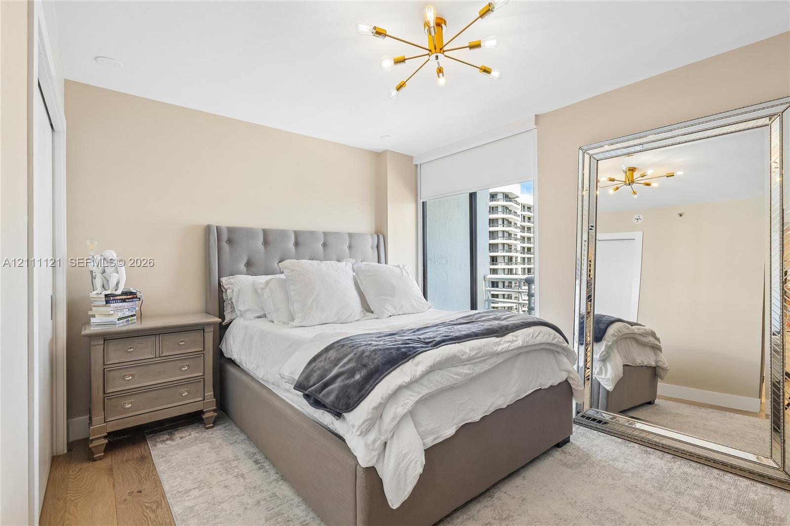 Gold-tone multi-arm chandelier, large floor-to-ceiling windows, roller shades, and wood-finish flooring