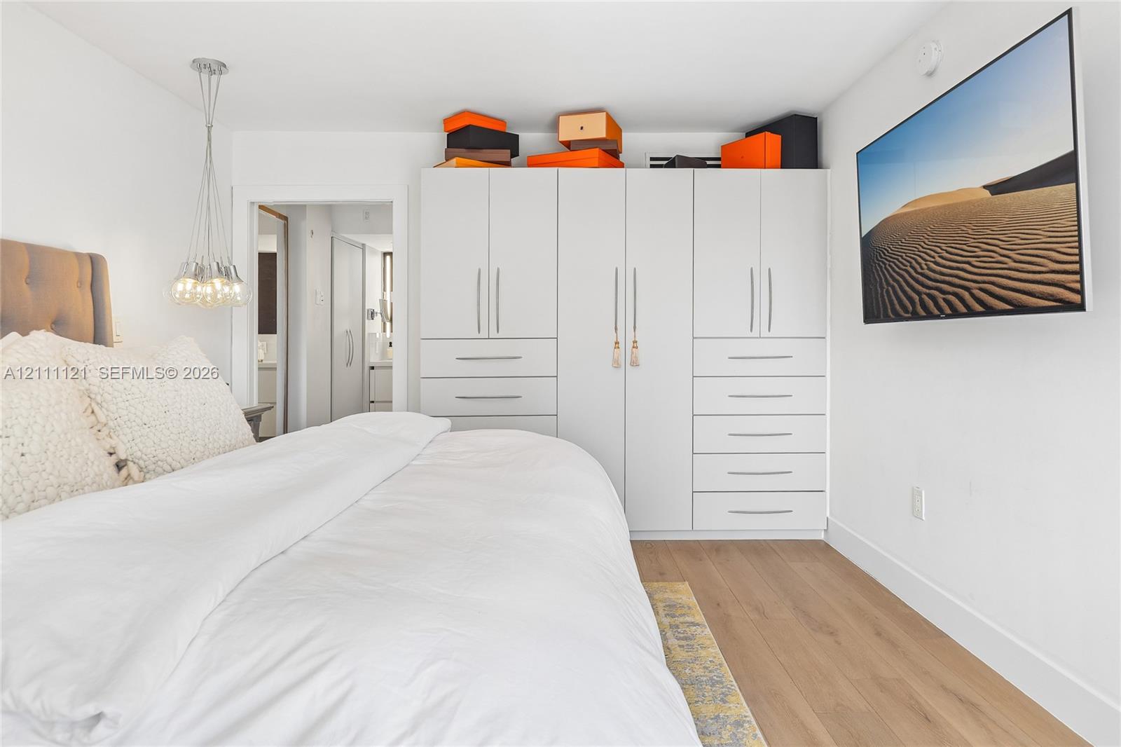 Built-in white floor-to-ceiling wardrobe with integrated drawers, wood-finish flooring, and a multi-bulb suspended pendant light fixture