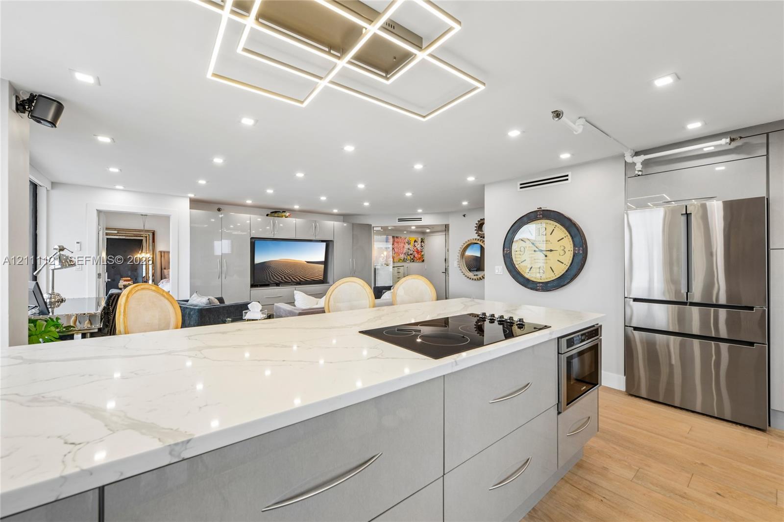Kitchen island featuring a stone-look countertop with an integrated induction cooktop, high-gloss cabinetry, wood-finish flooring, stainless steel multi-door refrigerator, and contemporary geometric recessed ceiling lighting