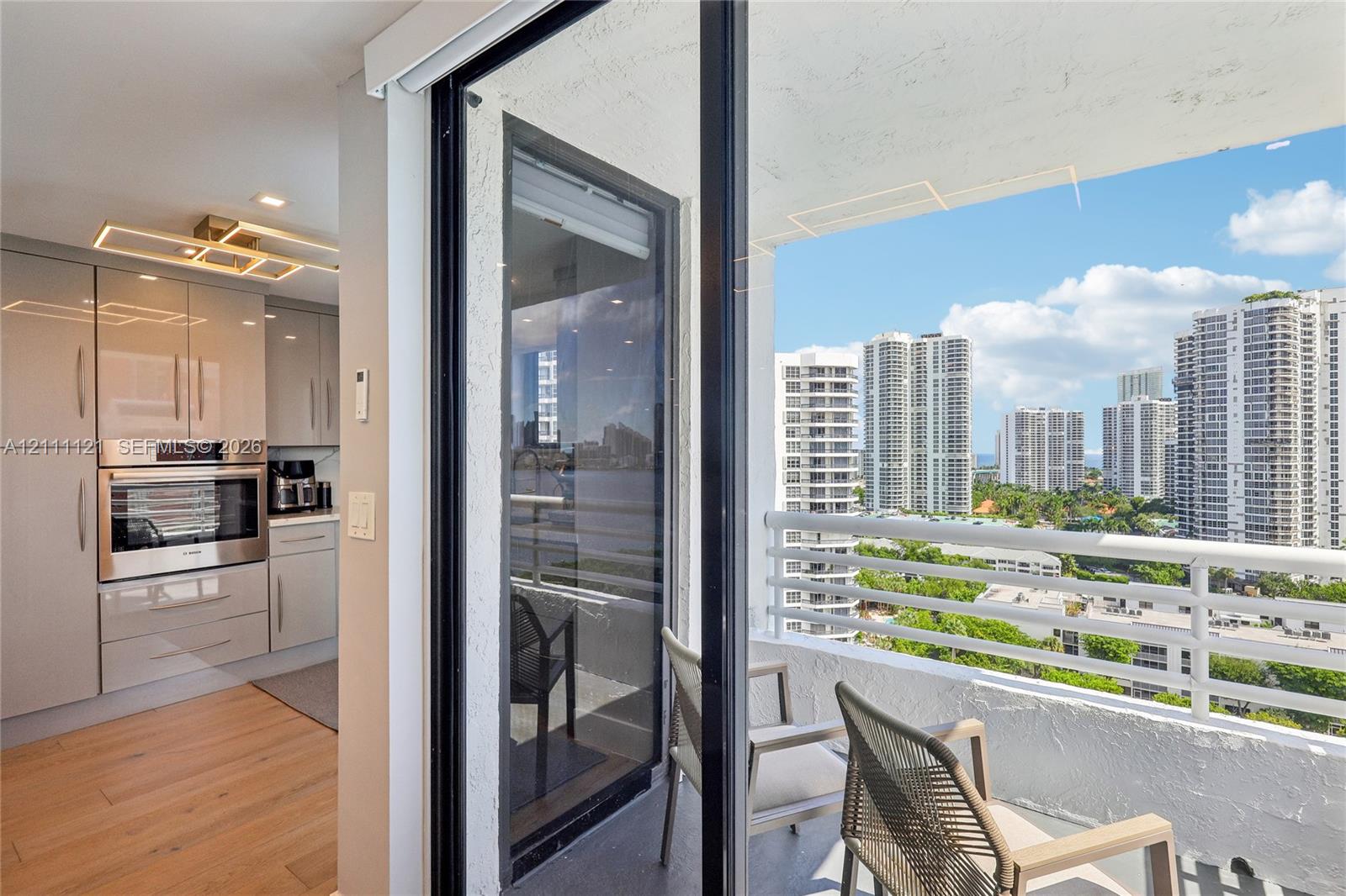 Kitchen featuring high-gloss cabinetry, stainless steel built-in wall oven, wood-finish flooring, and a balcony with a white metal railing and a cityscape backdrop