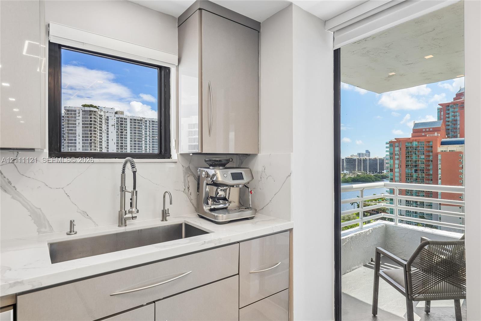 Glossy cabinetry featuring integrated hardware, stone-finish backsplash, undermount stainless steel sink with high-arc pull-down faucet, and access to a private balcony