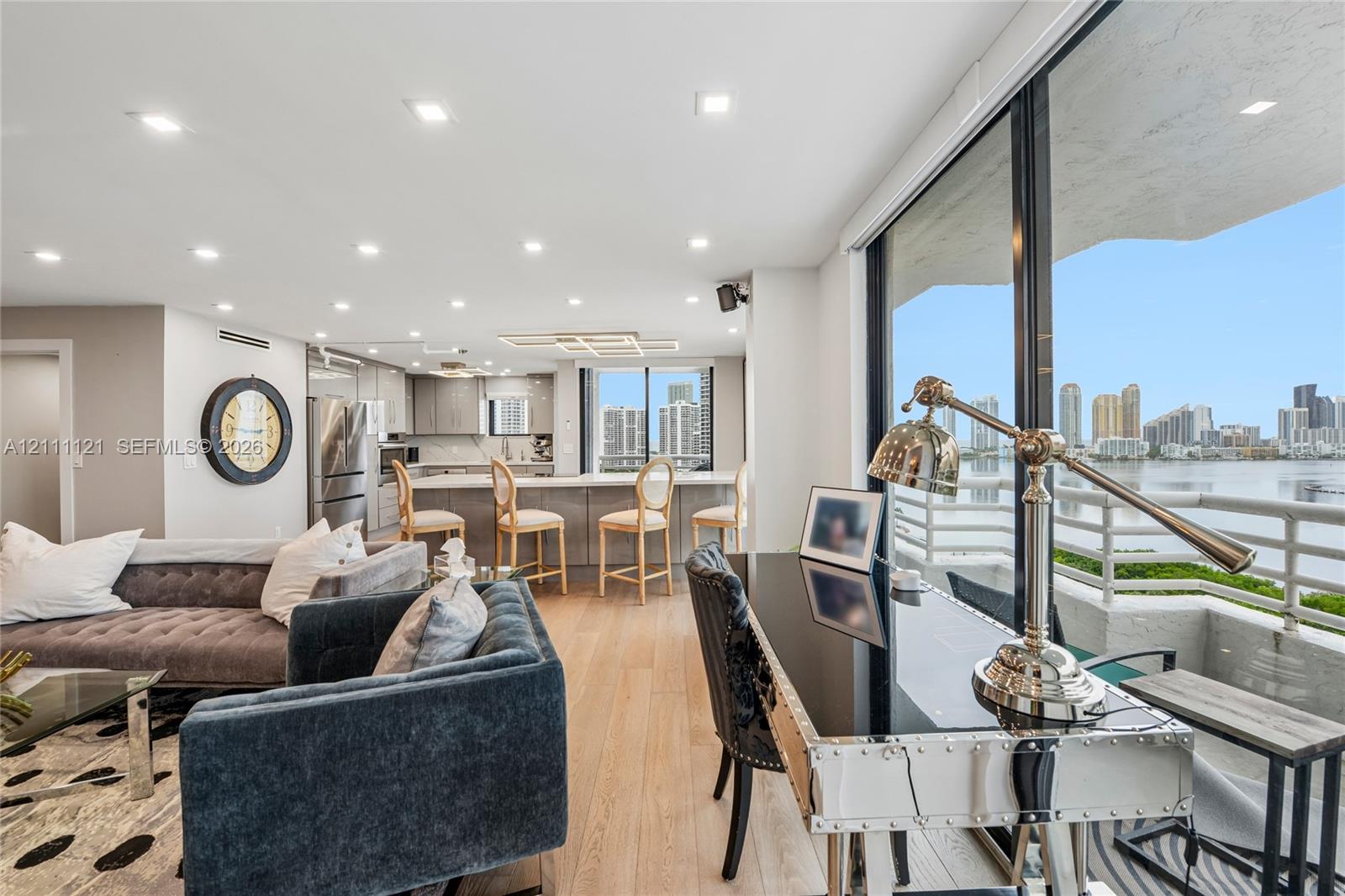 Open-concept interior featuring light-toned wood-finish flooring, recessed lighting, kitchen with stainless steel appliances and island, and expansive floor-to-ceiling glass wall