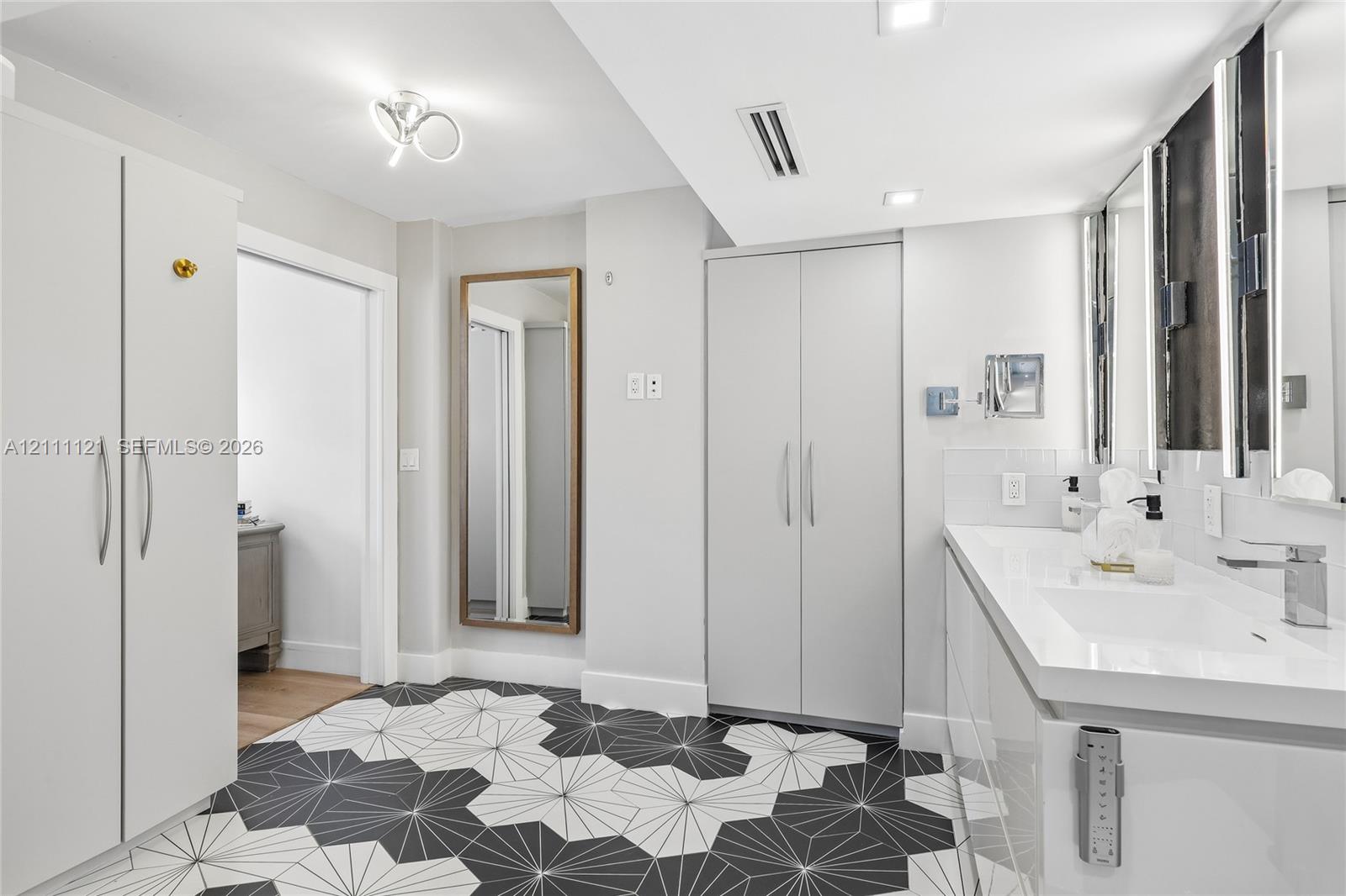 Bathroom featuring a white dual-sink vanity with an integrated countertop, geometric tile flooring, floor-to-ceiling white cabinetry, and recessed lighting