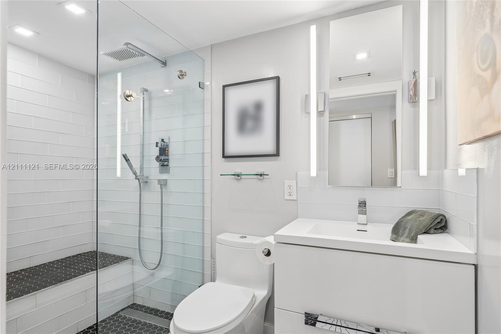 Walk-in shower with glass enclosure, integrated tile bench, dual-function showerhead, floating white vanity, and vertical LED-integrated vanity lighting