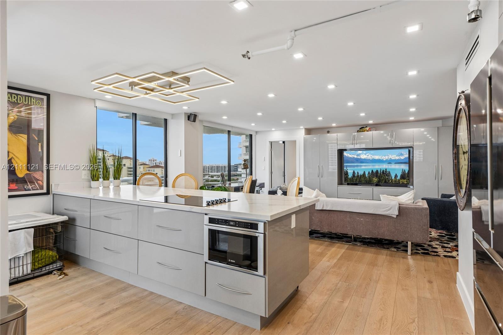 Modern kitchen featuring a central island with integrated cooktop and microwave, high-gloss cabinetry, stone-surface countertops, wood-finish flooring, and geometric LED ceiling lighting