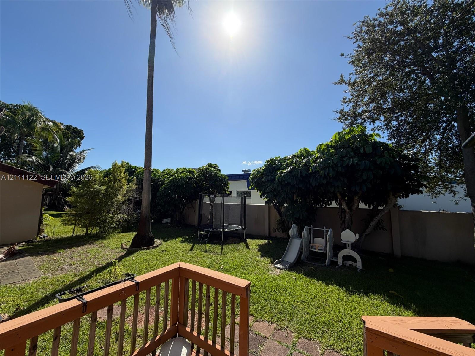 Backyard featuring a wood-rail deck, expansive lawn, mature trees, and a solid perimeter wall