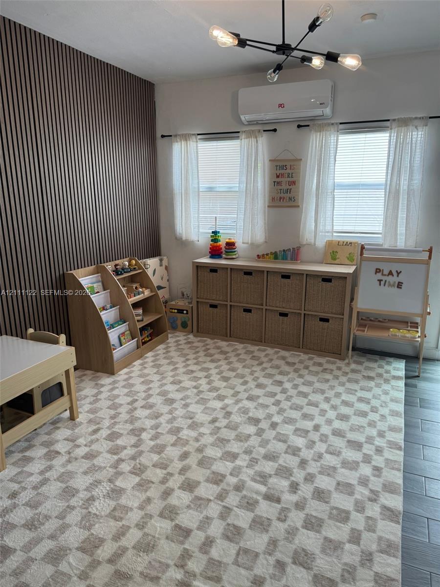 Vertical wood-slat accent wall, modern multi-arm light fixture, wall-mounted ductless HVAC unit, and neutral tile flooring