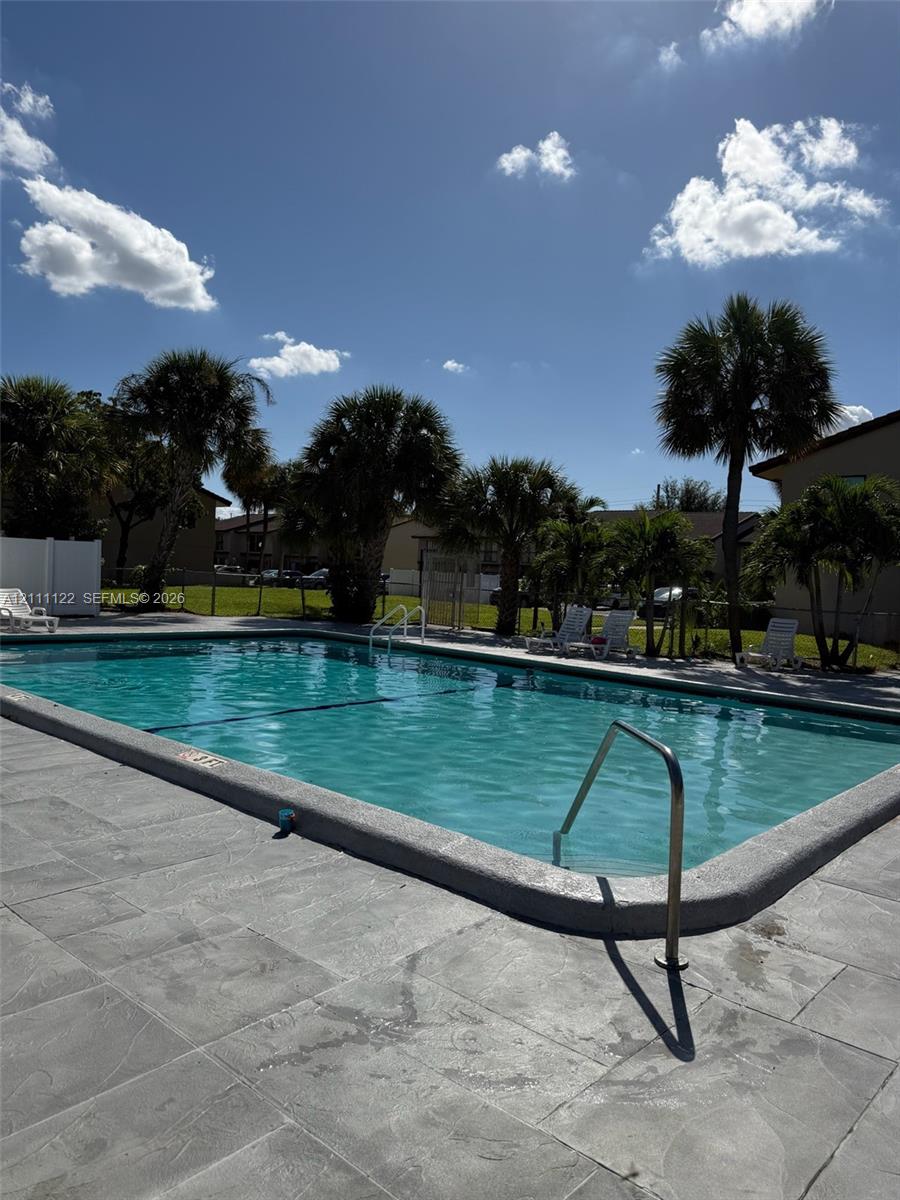 In-ground swimming pool featuring a concrete deck, metal handrails, and surrounding palm trees
