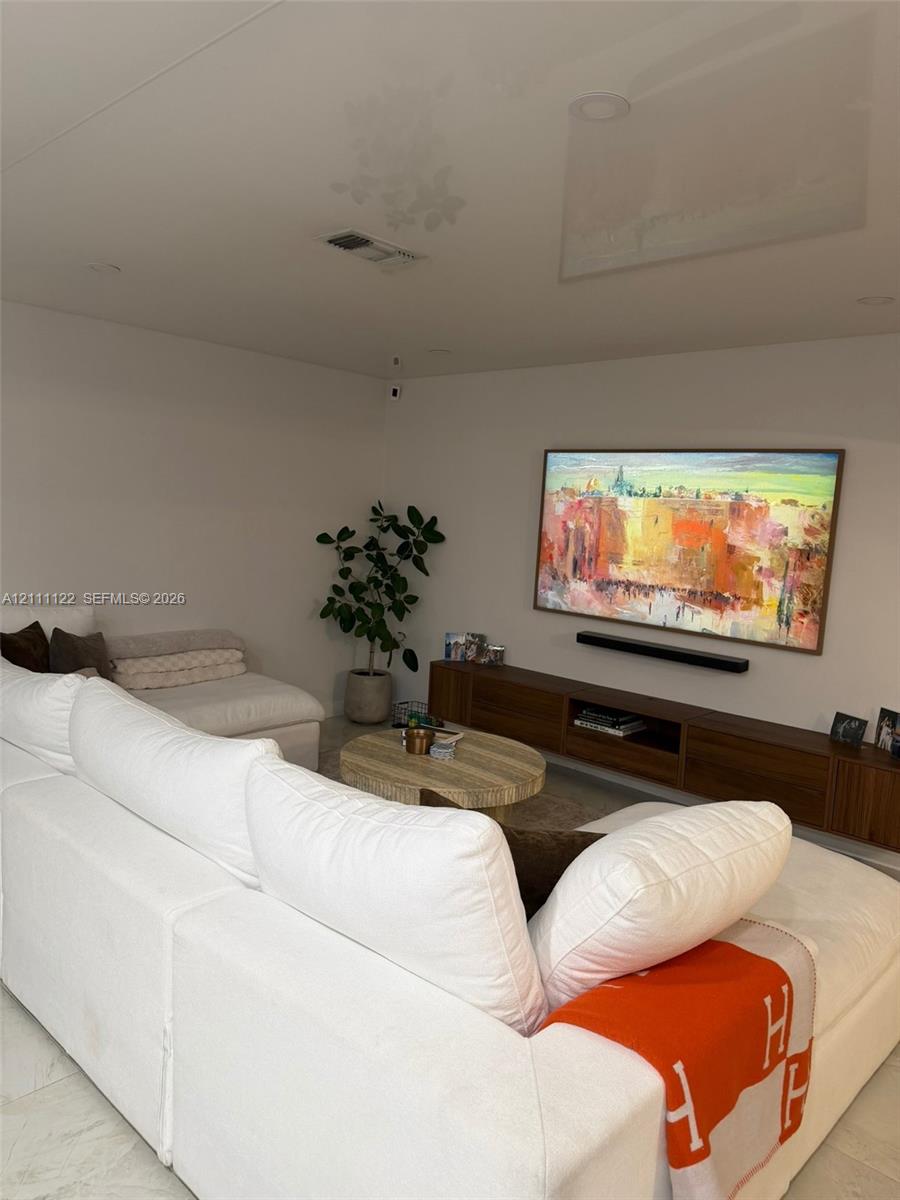 Wall-mounted wood-finish media console, recessed ceiling lighting, and neutral stone-finish flooring
