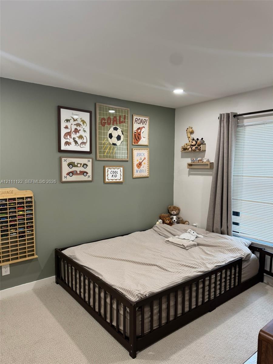 Neutral-toned interior space featuring a sage green accent wall, wall-to-wall carpeting, recessed ceiling lighting, and window with attached curtain rod and blinds