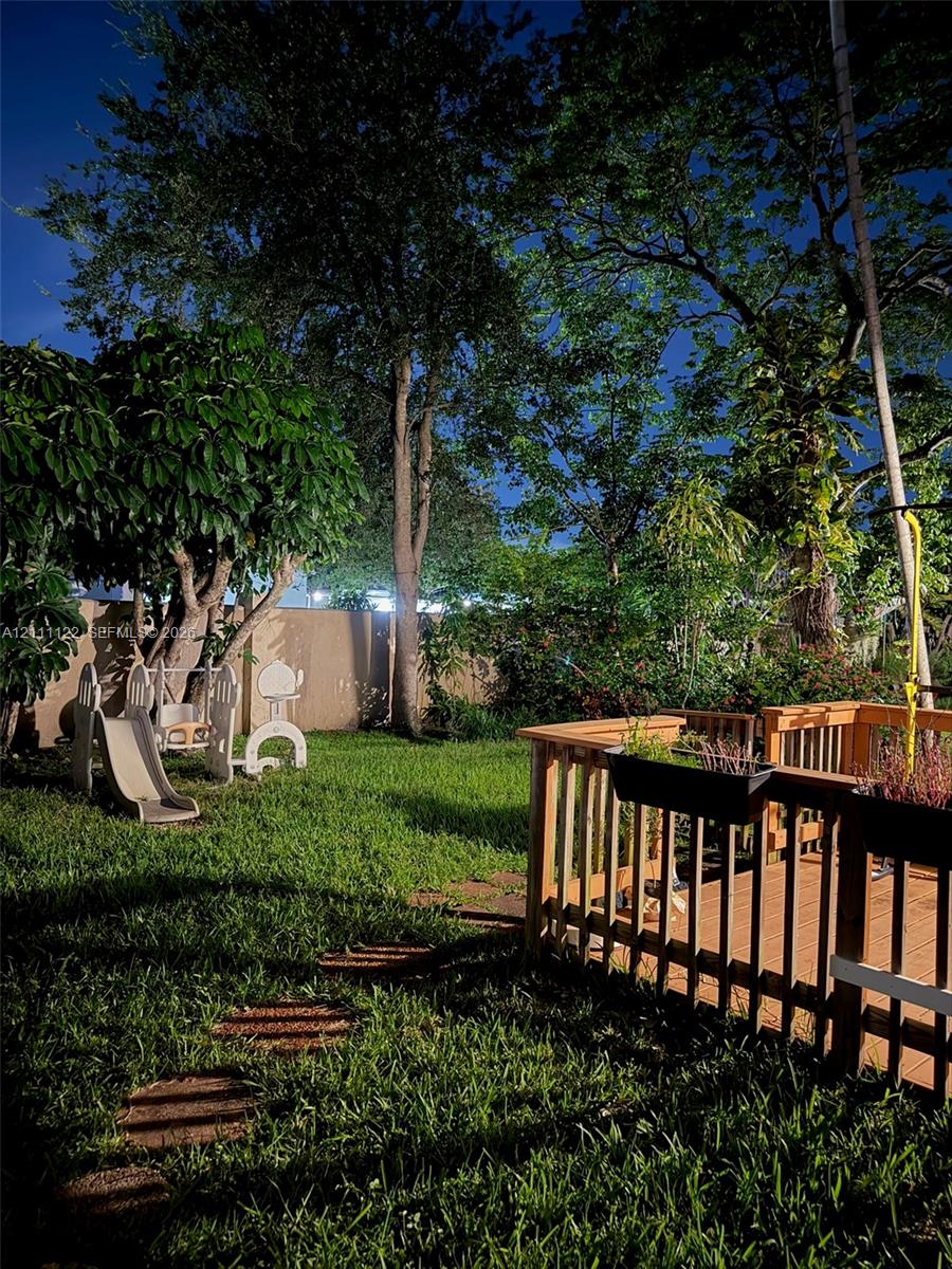Backyard featuring a wood-decked patio with integrated railing, stone paver path, solid perimeter fencing, and mature trees