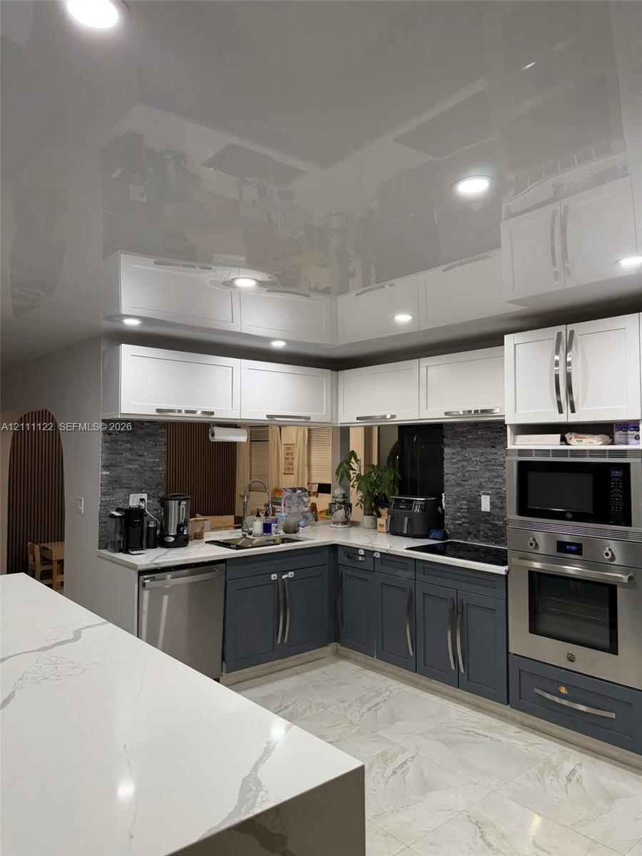 Kitchen featuring two-tone cabinetry, high-gloss ceiling finish, stone-surfaced countertops, stone-tile backsplash, and recessed lighting