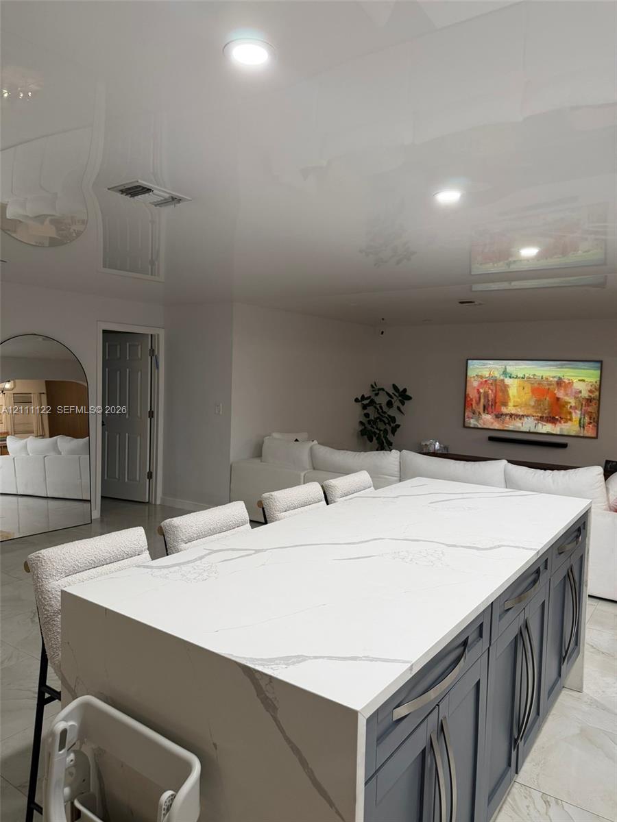 Kitchen island with a white stone countertop, waterfall edge, and dark cabinetry