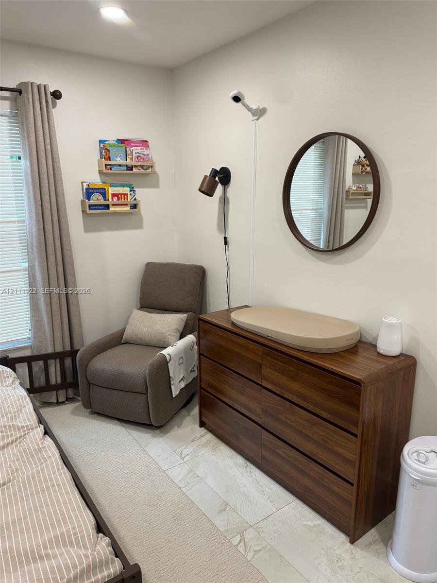 Wall-mounted light fixture, circular wall mirror with dark finish, and neutral stone-finish flooring