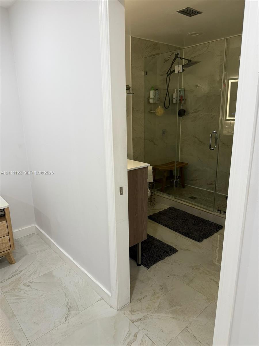 Bathroom featuring stone-finish flooring, a wood-finish vanity, and a glass-enclosed shower with a rainfall showerhead