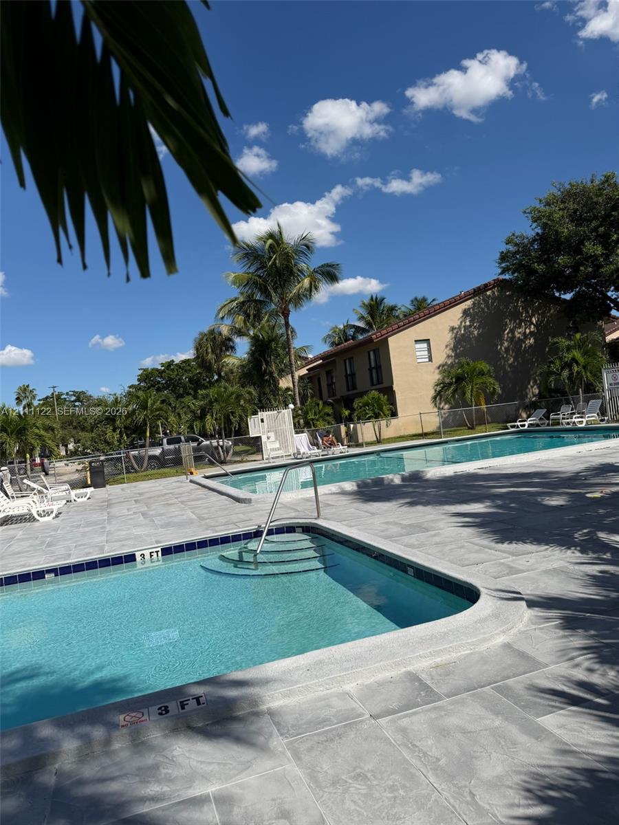 In-ground swimming pool with built-in stairs, metal handrail, and stone-tiled pool deck