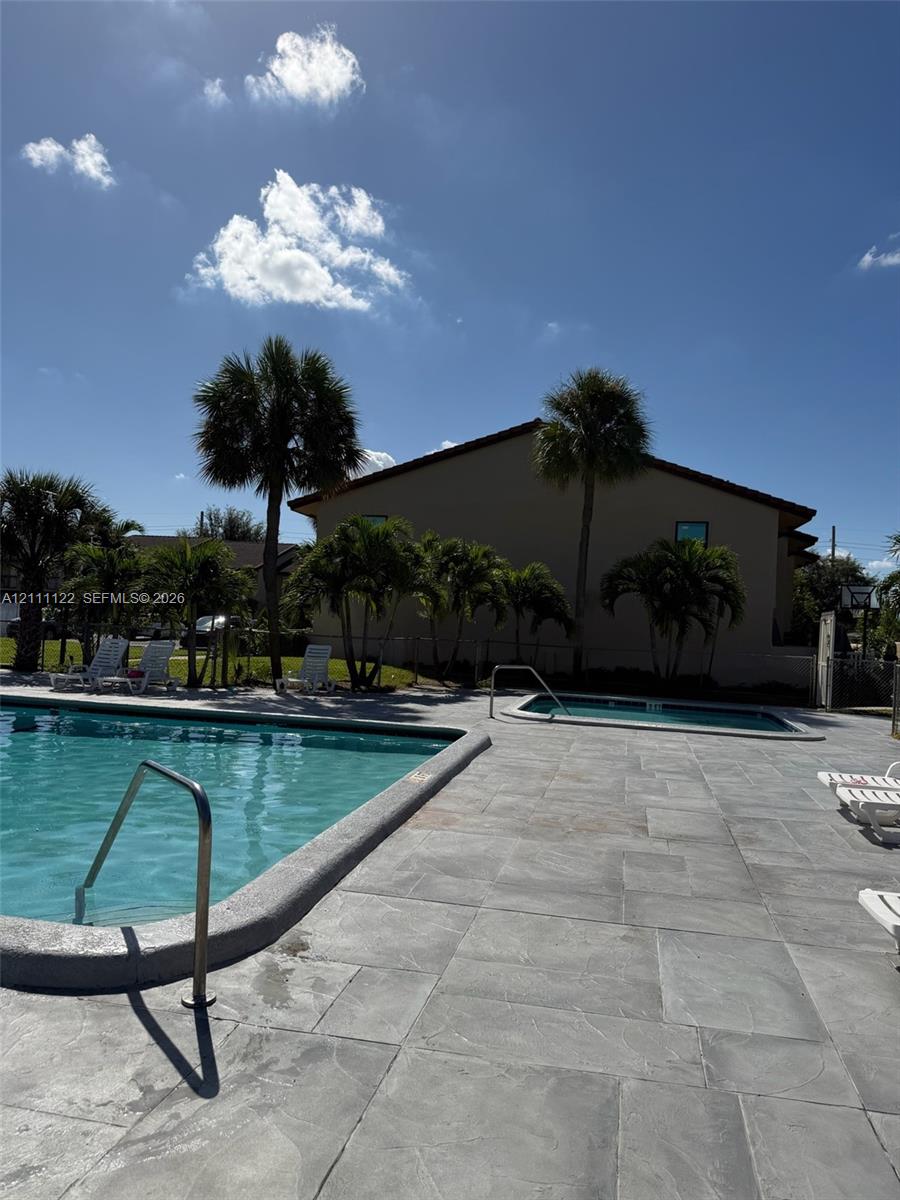Outdoor pool and hot tub area featuring concrete paver decking, metal handrails, and mature palm trees