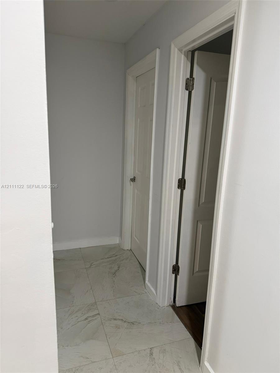Large-format, stone-finish floor tiling with neutral veining, paired with white interior doors featuring classic panel detailing and polished metal hardware