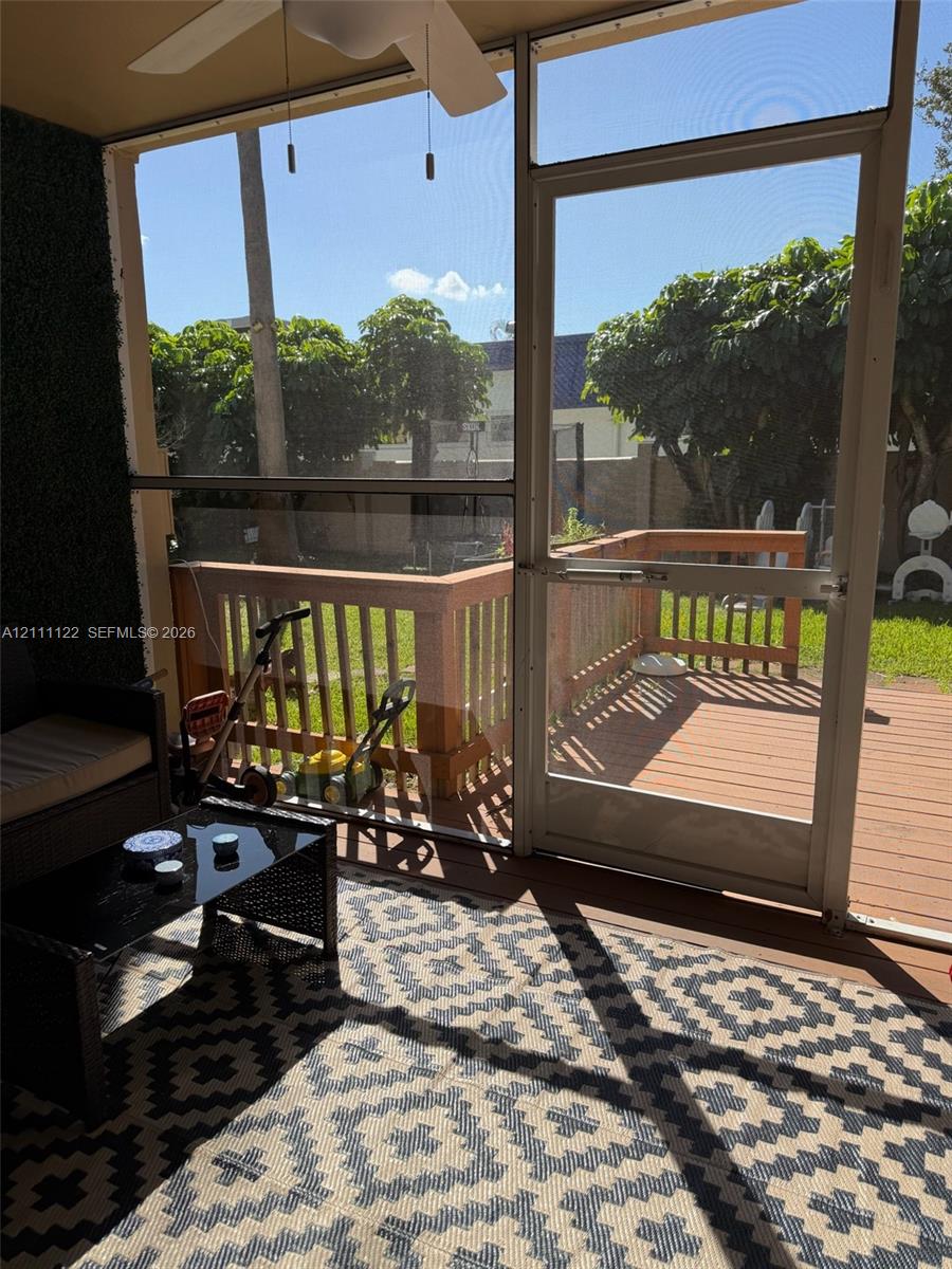 Screened-in porch featuring a ceiling fan, wood-toned deck, metal railings, and a direct-entry screen door
