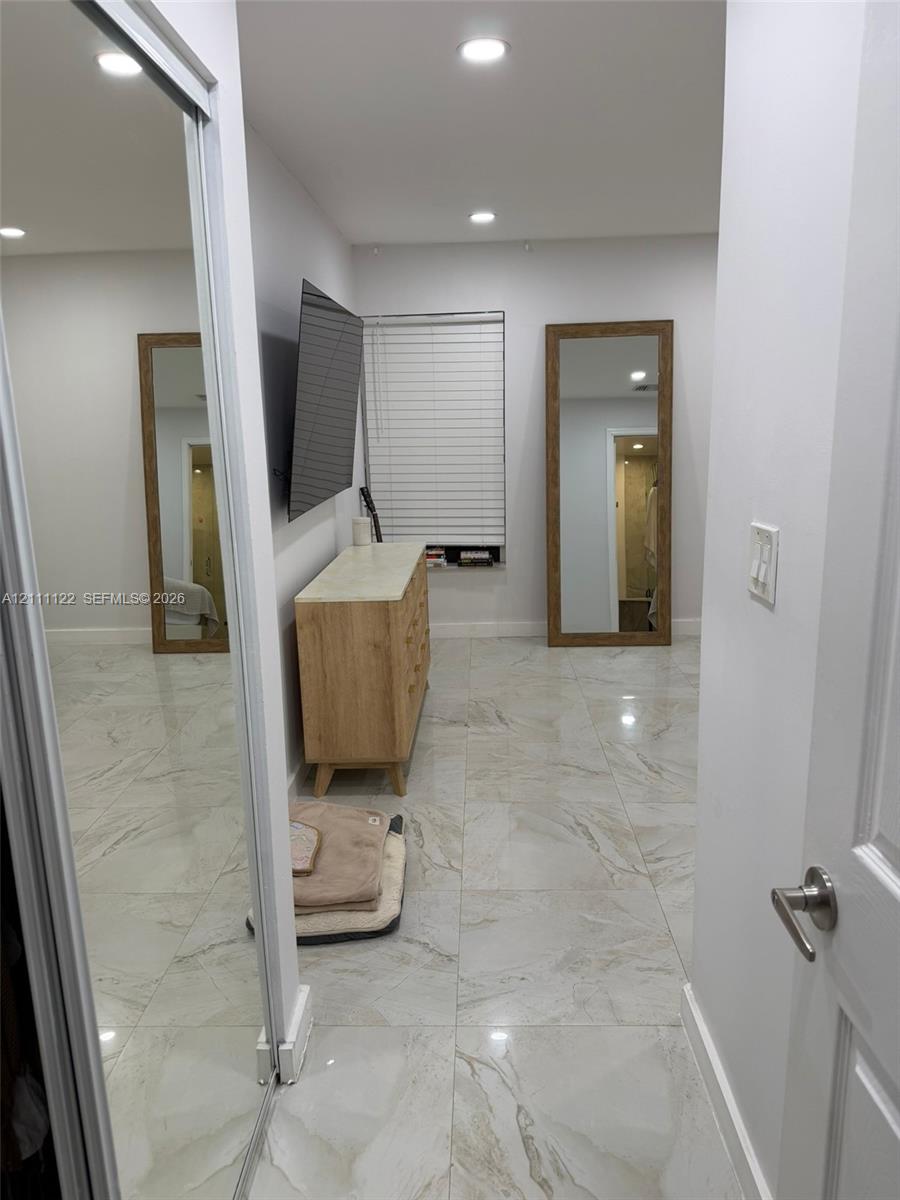 Neutral-toned large-format tile flooring, recessed ceiling lighting, sliding mirrored closet doors, and horizontal window blinds