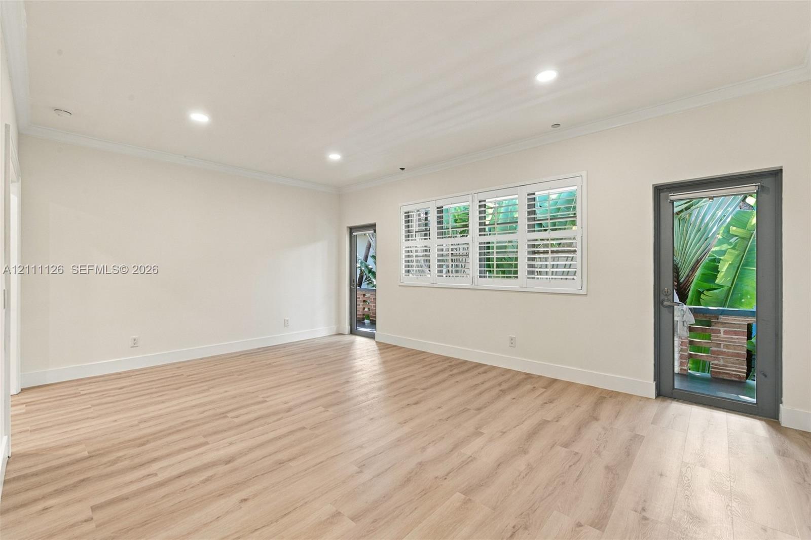 Spacious room featuring wood-finish flooring, recessed lighting, multi-pane windows with plantation shutters, and glass-paneled exterior doors