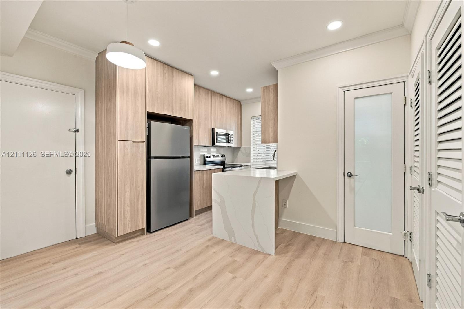 Kitchen featuring wood-finish cabinetry, stainless steel appliances, a waterfall-edge stone countertop, recessed lighting, and wood-finish flooring
