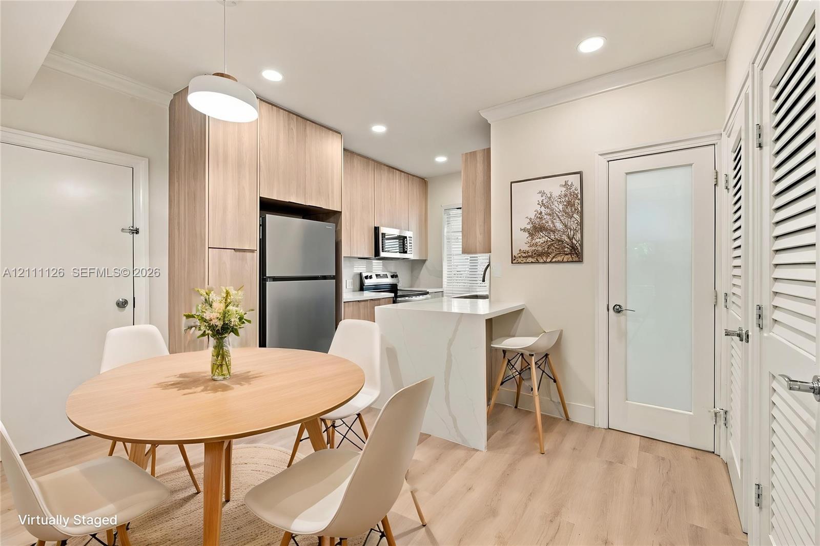 Kitchen featuring light wood-finish cabinetry, stone-surface breakfast bar, stainless steel appliances, and wood-finish flooring