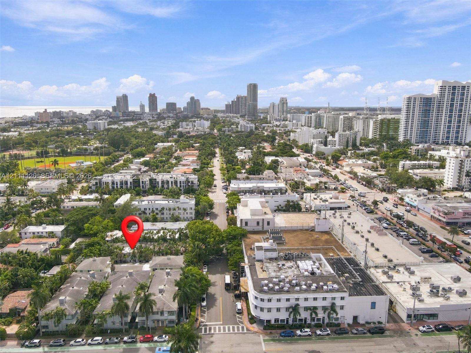 Aerial perspective of a multi-unit property featuring a flat roofline, mature palms, dense surrounding greenery, and proximity to metropolitan infrastructure