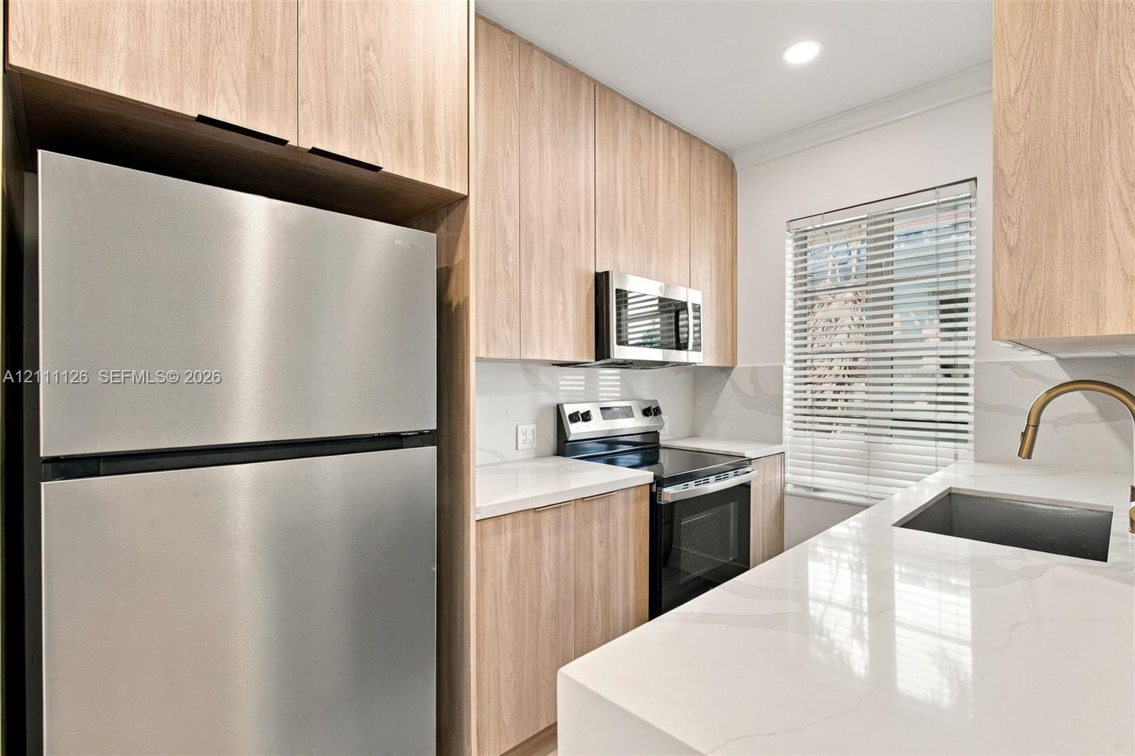 Kitchen featuring light wood-finish cabinetry, white stone-surfaced countertops, a stainless steel refrigerator, a built-in microwave, and a gooseneck faucet