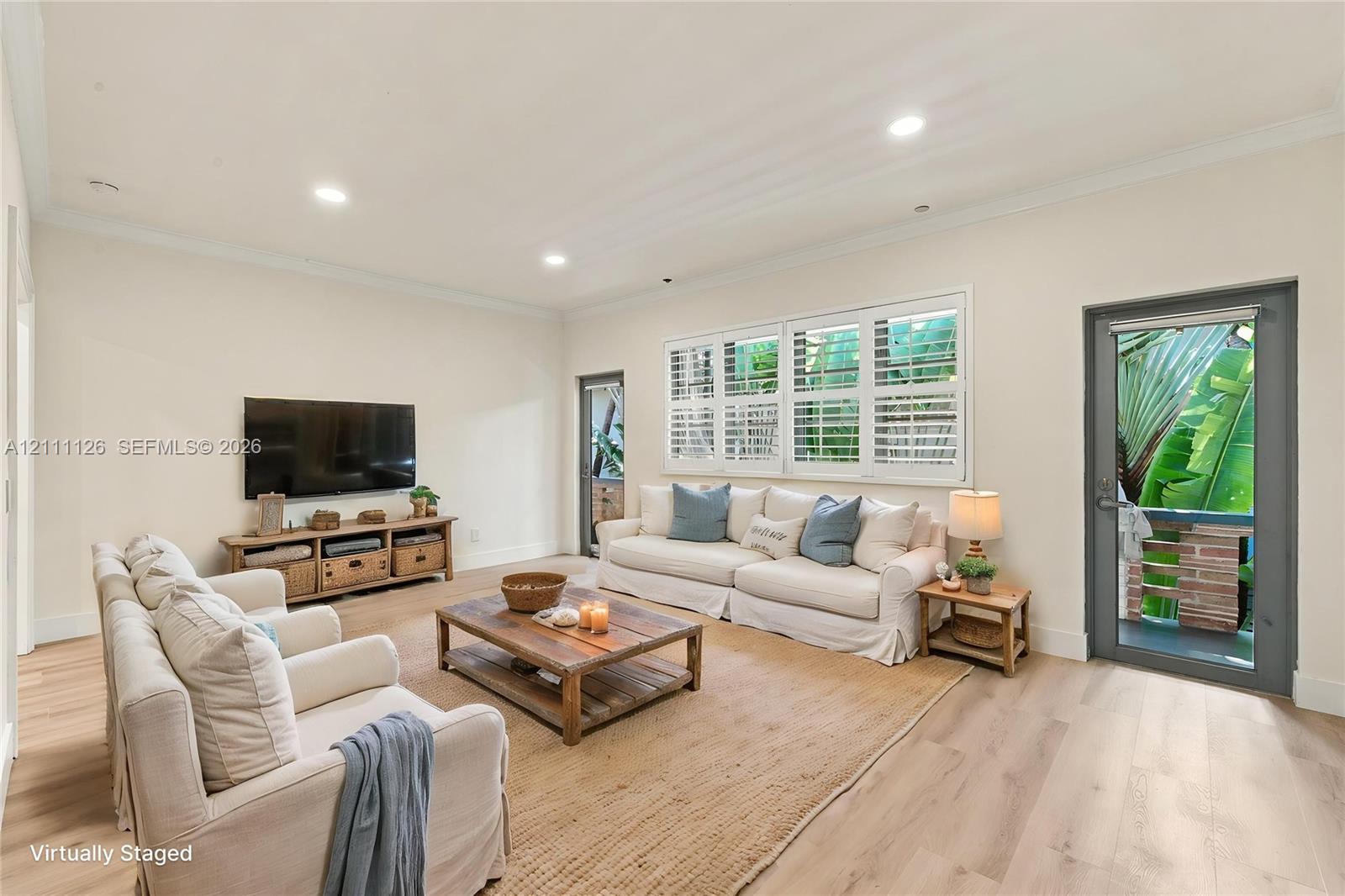 Living area featuring light-toned wood-finish flooring, recessed lighting, crown molding, multi-pane windows with plantation shutters, and two full-lite exterior doors Living area featuring light-toned wood-finish flooring, recessed lighting, crown molding, multi-pane windows with plantation shutters, and two full-lite exterior doors