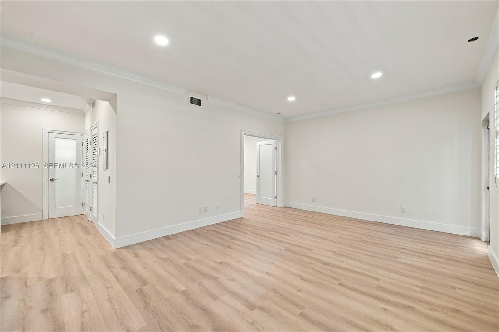 Spacious room featuring wood-finish flooring, recessed lighting, crown molding, and neutral wall color