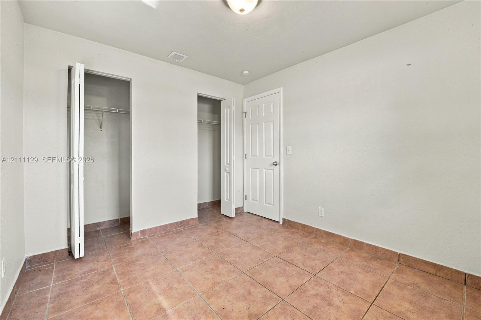 Interior room featuring large-format ceramic tile flooring, two closets with bi-fold doors, and a paneled interior door with a brushed-metal knob