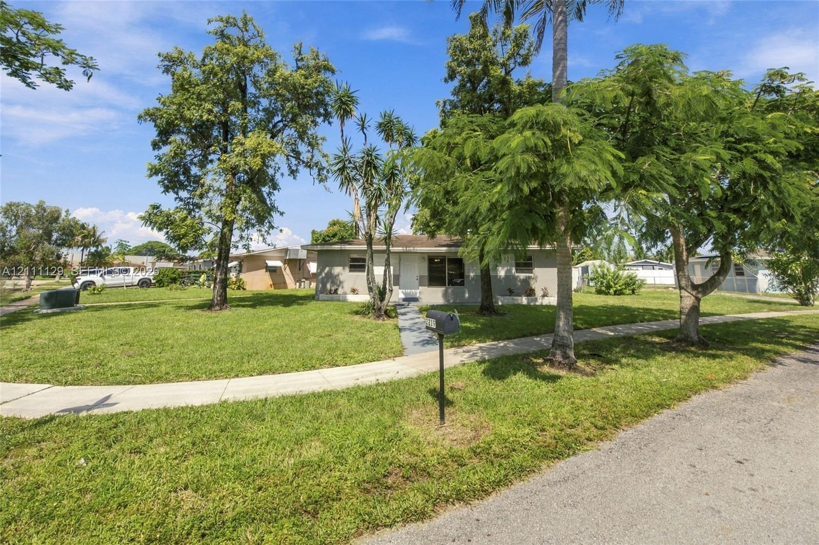 Single-story residence featuring a light-toned exterior, concrete walkway, and mature landscaping situated on a spacious grass lawn