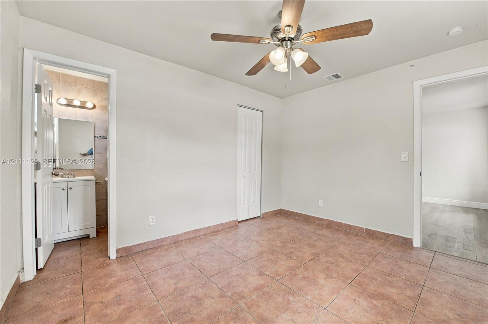 Neutral-toned room featuring tile flooring, a multi-blade ceiling fan with integrated lighting, and a bi-fold closet door