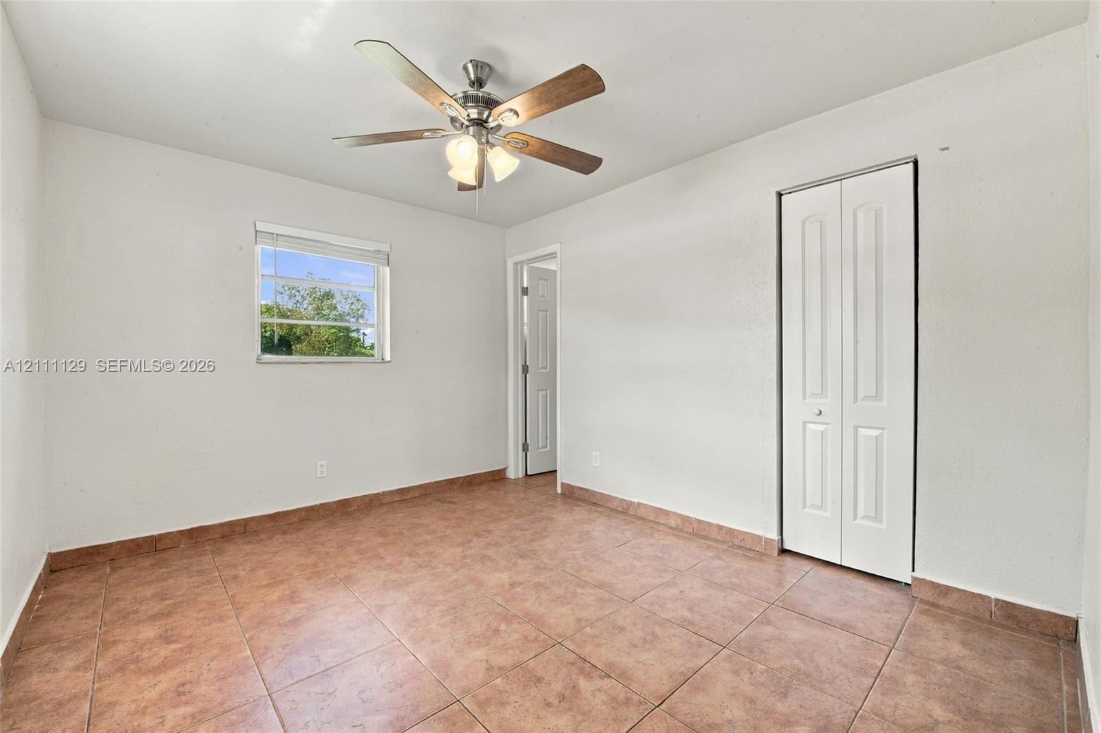 Room featuring ceramic tile flooring, a multi-blade ceiling fan with integrated light fixture, a single-hung window, and a white bifold closet door