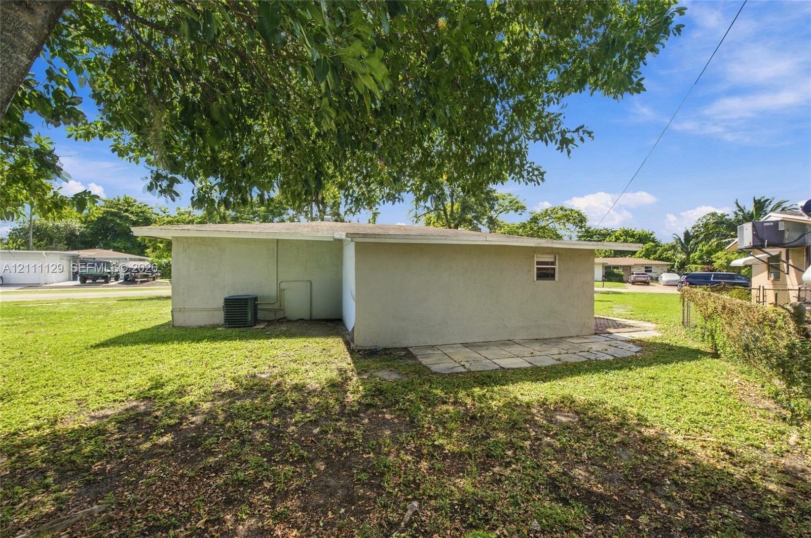 Stucco exterior dwelling featuring a concrete slab patio, sprawling lawn, and mature shade trees