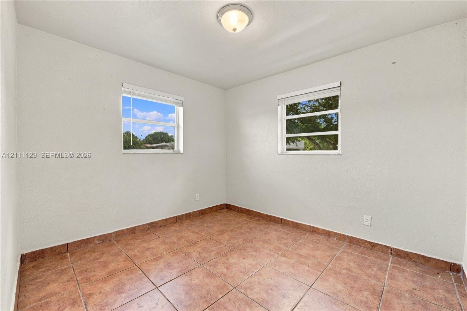 Neutral-toned room featuring tiled flooring, two double-hung windows, and a flush-mount ceiling light fixture