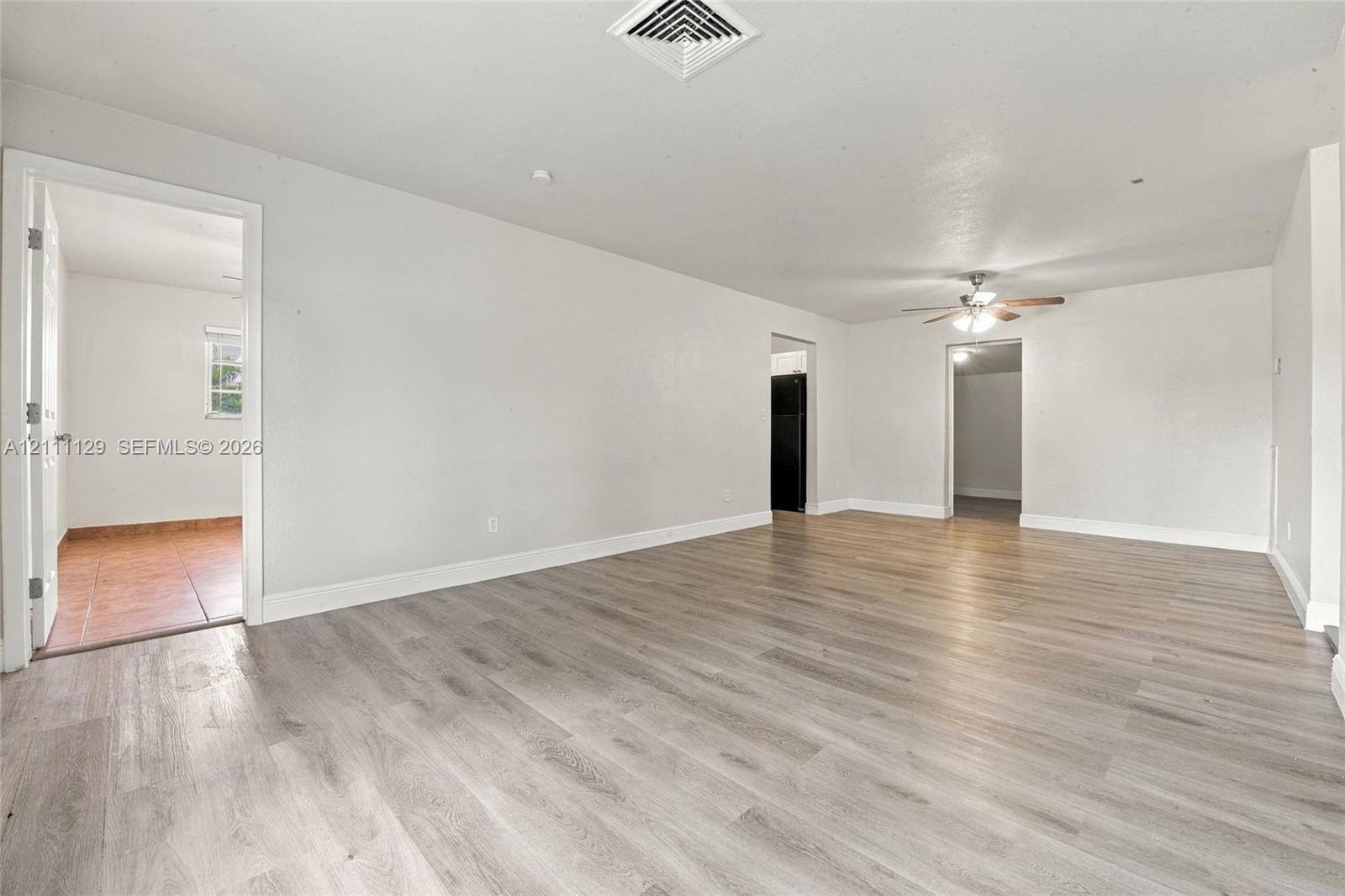 Open-concept interior featuring light wood-finish flooring, neutral wall tones, and a ceiling fan with integrated lighting
