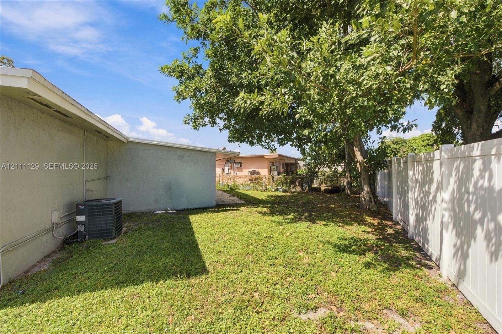 Backyard area featuring a vinyl privacy fence, mature shade trees, and a grass lawn