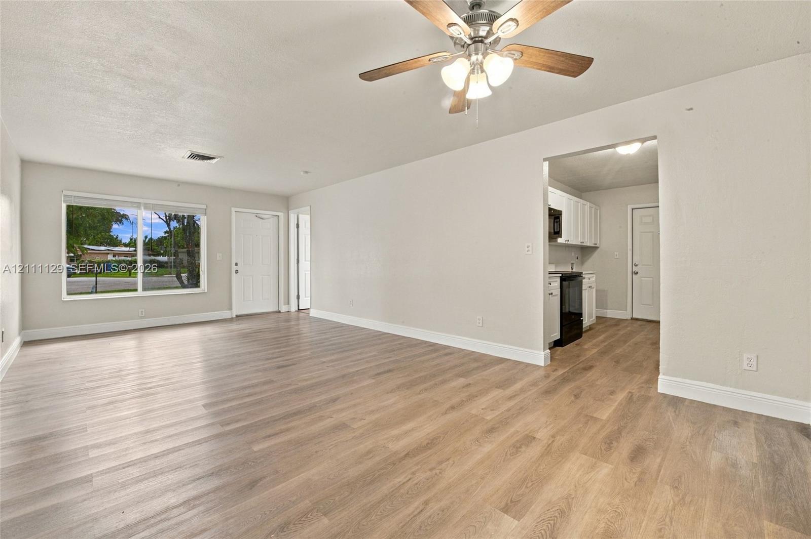 Open interior featuring wood-finish flooring, a ceiling fan with integrated lighting, and white cabinetry