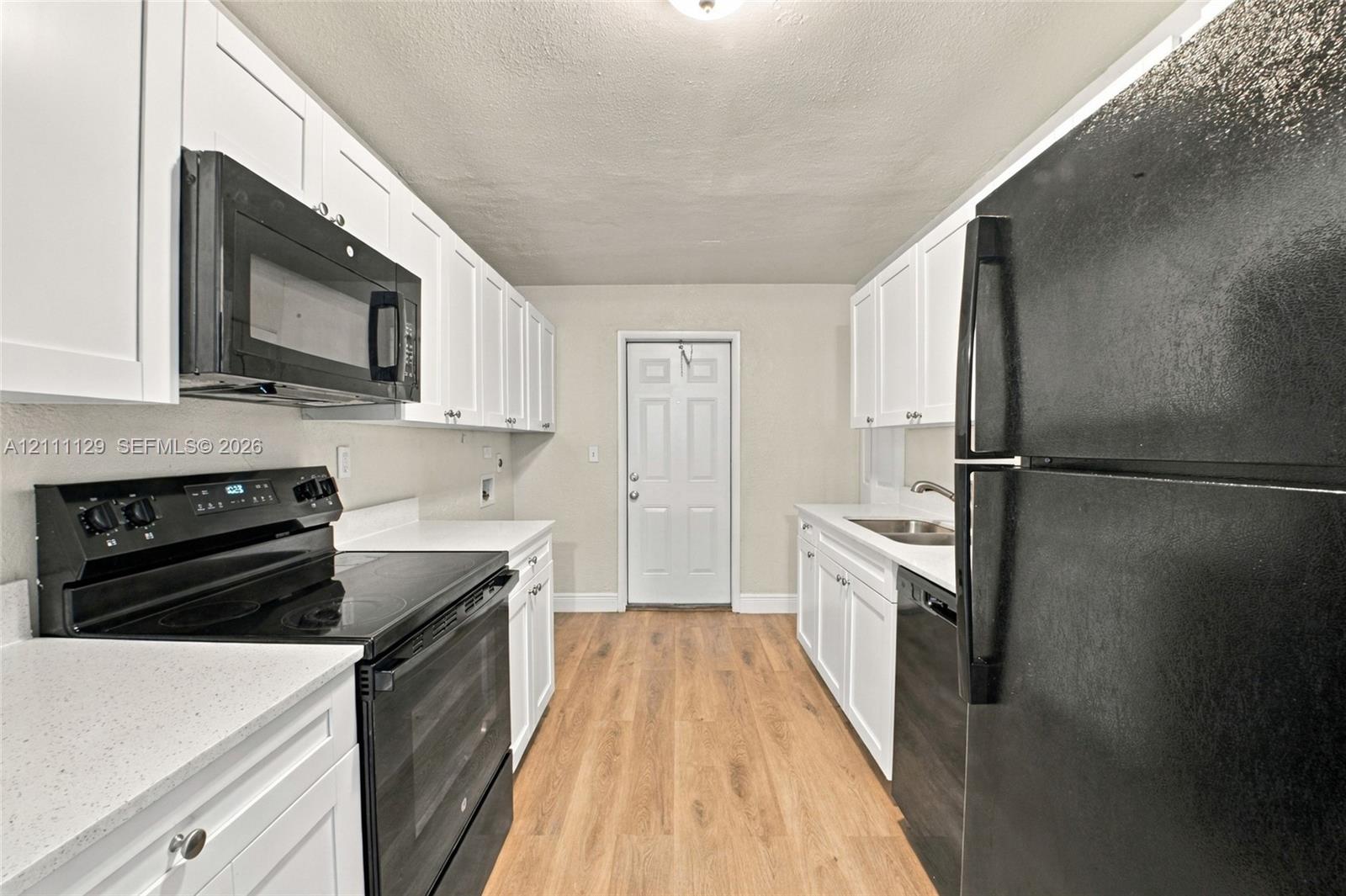 Kitchen featuring white shaker-style cabinetry, light-toned wood-finish flooring, solid surface countertops, and black built-in appliances