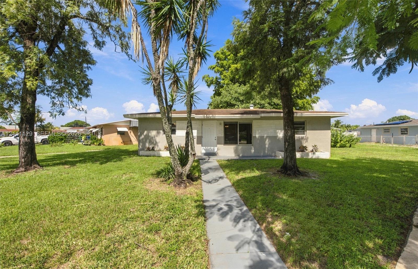 Single-story exterior featuring a painted masonry facade, a straight concrete walkway, and mature trees across a grass lawn Single-story exterior featuring a painted masonry facade, a straight concrete walkway, and mature trees across a grass lawn