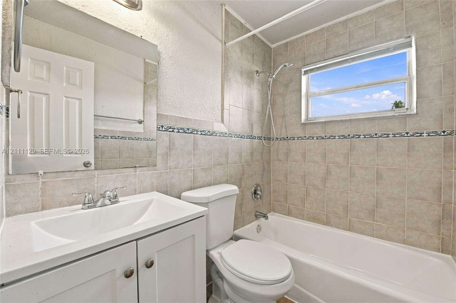 Bathroom featuring a white vanity cabinet, square undermount sink, tiled shower surround with decorative inlay, and a built-in bathtub with a handheld shower fixture
