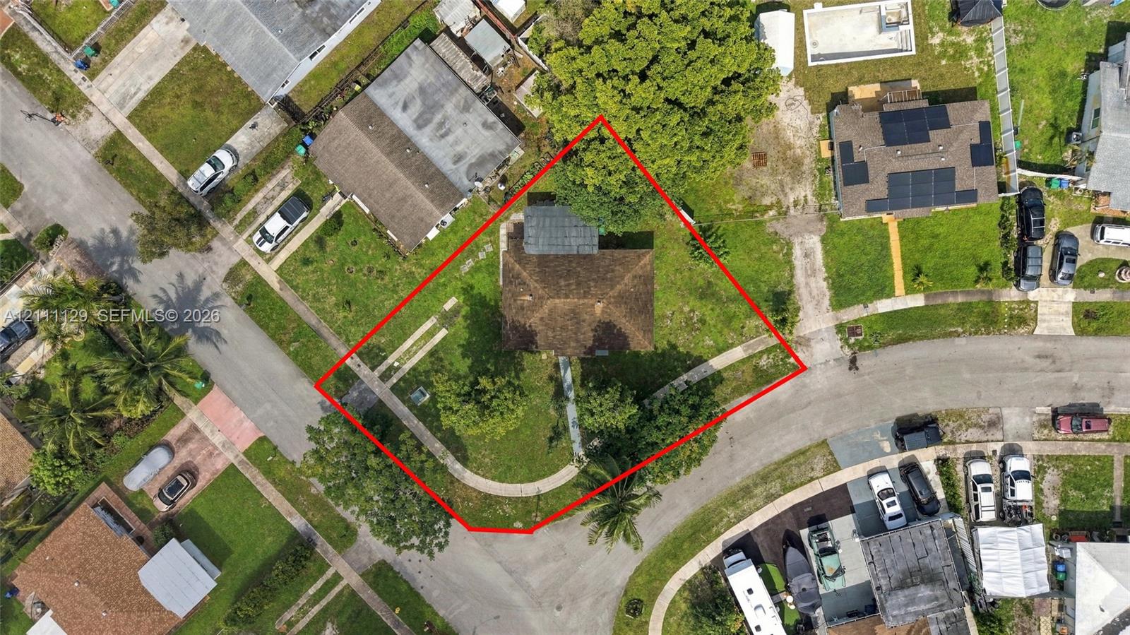 Aerial perspective of a corner lot featuring a hipped roof structure, curved concrete walkway, mature trees, and ample green space