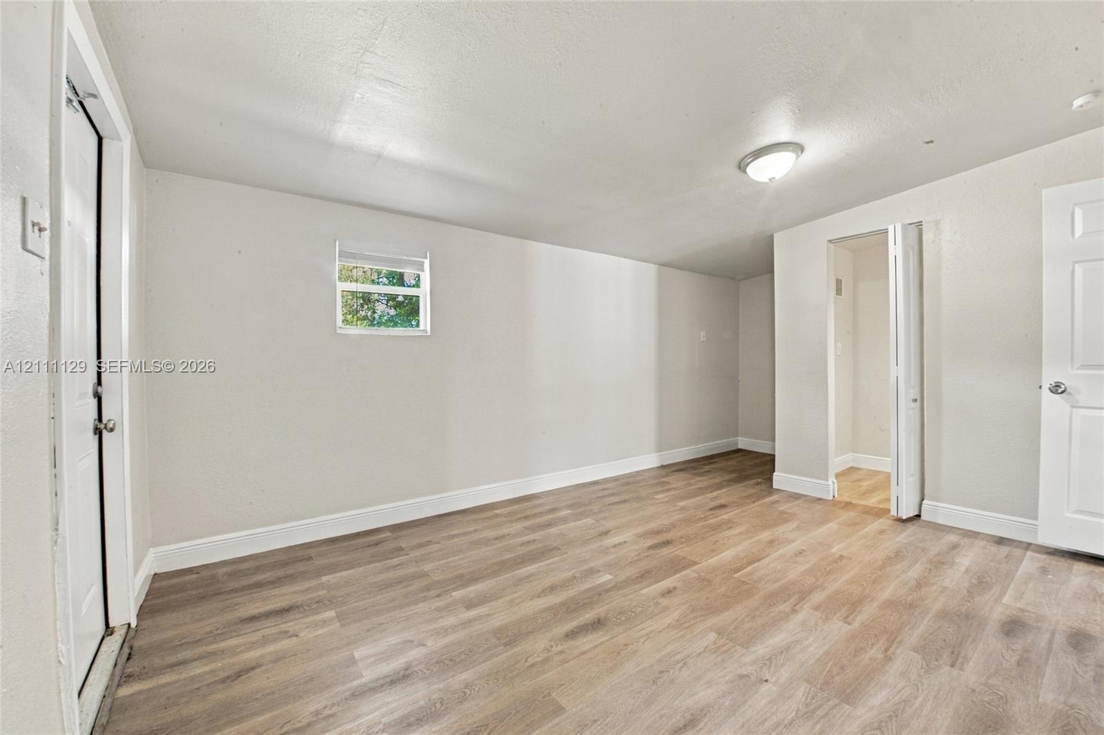 Interior space featuring light-toned wood-finish flooring, neutral wall paint, a flush-mount ceiling light, a single-pane window, and white interior doors